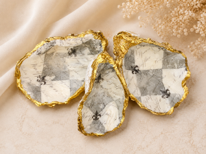Decorative gold-rimmed ceramic shells with a black-and-white checker pattern resting on beige fabric and dried flowers in the corner.