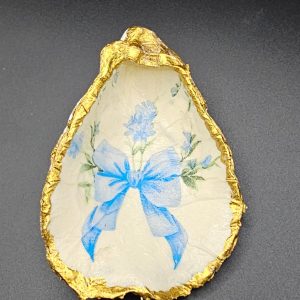 Decorative egg-shaped object with blue floral pattern and gold foil edging on a dark surface.