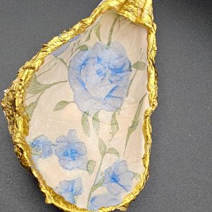 A torn piece of floral wallpaper with blue flowers and green leaves, framed by crinkled gold foil edging.