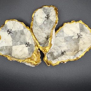 Three irregular geode slices with gold leaf along their rough edges laid on a dark background; resembles decorative stones.