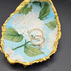 A decorative gold-edged shell holding two gold wedding rings on a blue floral lining.